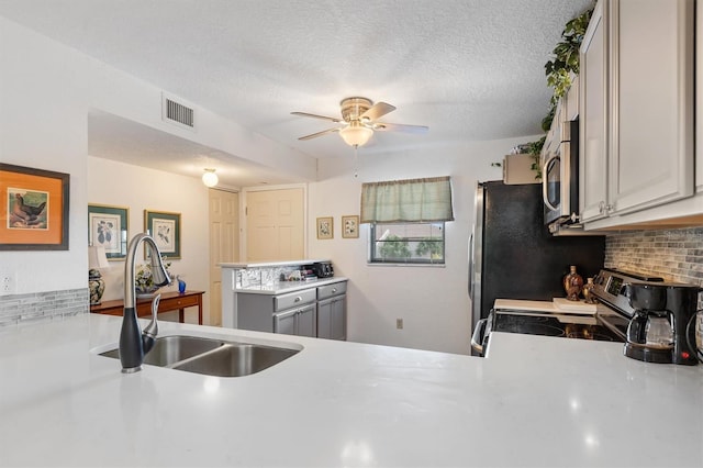 kitchen featuring gray cabinetry, backsplash, stainless steel appliances, ceiling fan, and sink