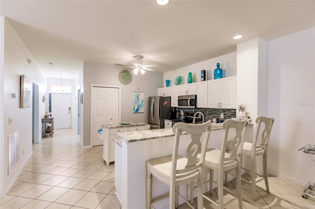 kitchen with appliances with stainless steel finishes, white cabinets, kitchen peninsula, a kitchen bar, and ceiling fan