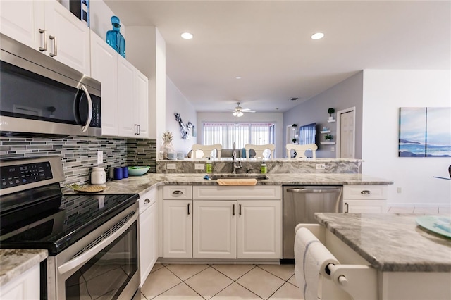 kitchen with appliances with stainless steel finishes, white cabinetry, ceiling fan, and light stone counters