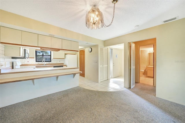 kitchen featuring cream cabinetry, decorative backsplash, white appliances, a textured ceiling, and light carpet