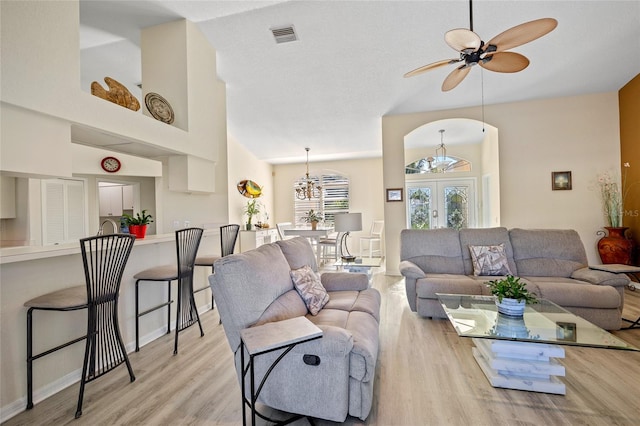 living room featuring french doors, light hardwood / wood-style flooring, high vaulted ceiling, and ceiling fan with notable chandelier