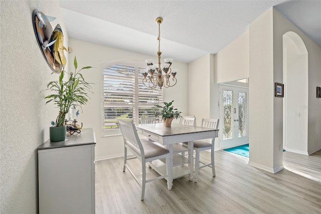 dining area with french doors, light hardwood / wood-style flooring, a chandelier, and a textured ceiling