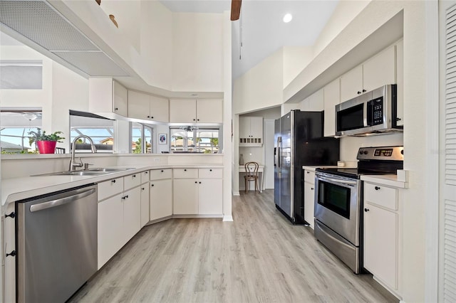 kitchen featuring a towering ceiling, stainless steel appliances, white cabinetry, and sink