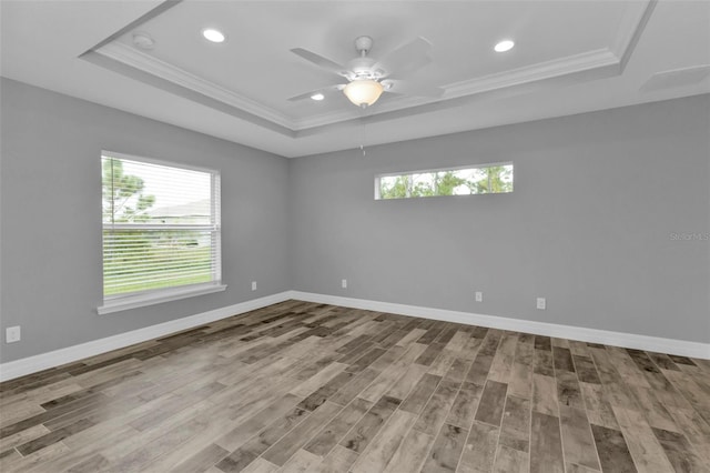 empty room featuring light wood-type flooring, ornamental molding, a tray ceiling, and ceiling fan