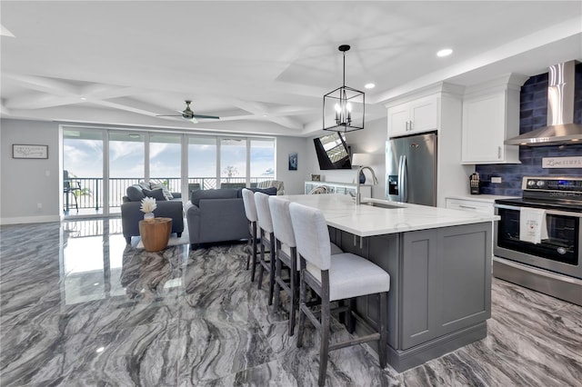 kitchen featuring sink, a kitchen island with sink, wall chimney exhaust hood, white cabinetry, and appliances with stainless steel finishes