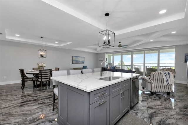 kitchen featuring light stone counters, a breakfast bar area, an island with sink, sink, and gray cabinetry