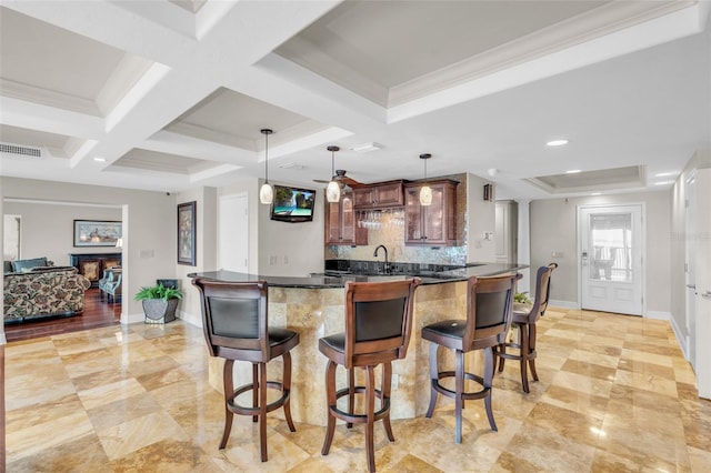 kitchen with coffered ceiling, backsplash, pendant lighting, crown molding, and a kitchen bar