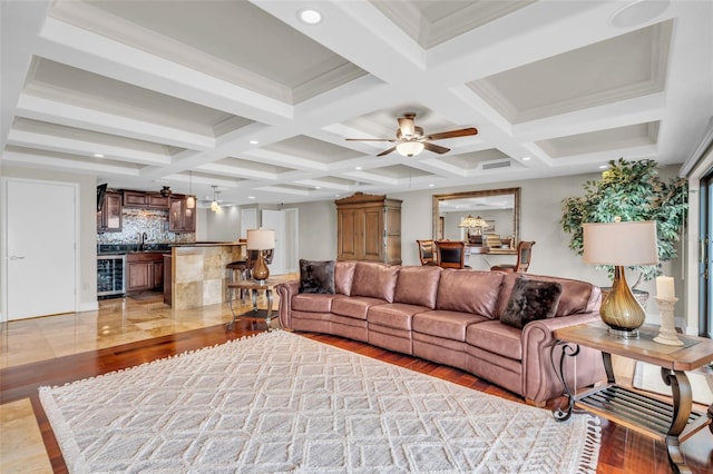 living room featuring coffered ceiling, beamed ceiling, light wood-type flooring, ceiling fan, and ornamental molding