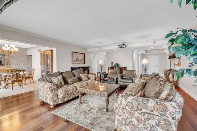 living room with wood-type flooring, ceiling fan with notable chandelier, crown molding, and decorative columns