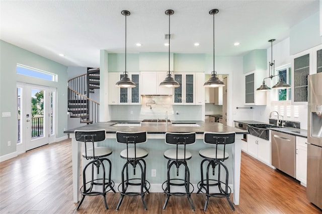 kitchen with white cabinetry, decorative light fixtures, a center island, light hardwood / wood-style flooring, and appliances with stainless steel finishes