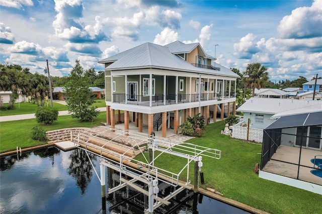 back of property with a balcony, a water view, glass enclosure, boat lift, and a yard