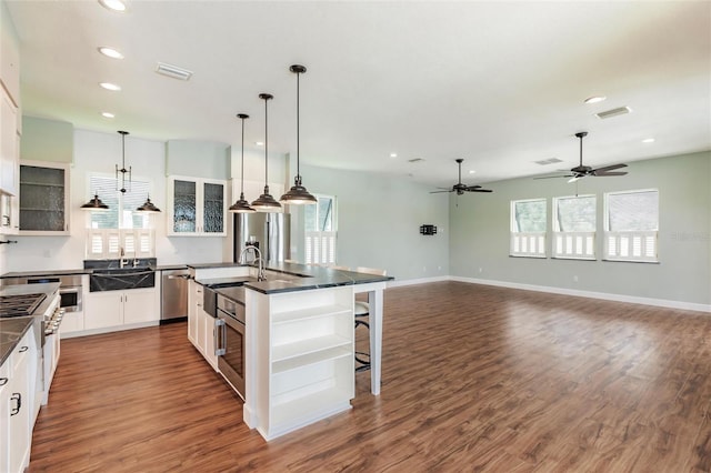 kitchen featuring dark wood-style flooring, dark countertops, an island with sink, white cabinets, and appliances with stainless steel finishes