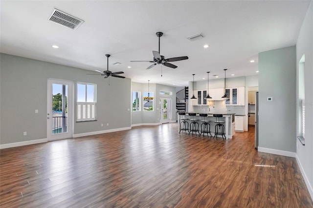 unfurnished living room featuring a healthy amount of sunlight, ceiling fan with notable chandelier, visible vents, and dark wood-style floors