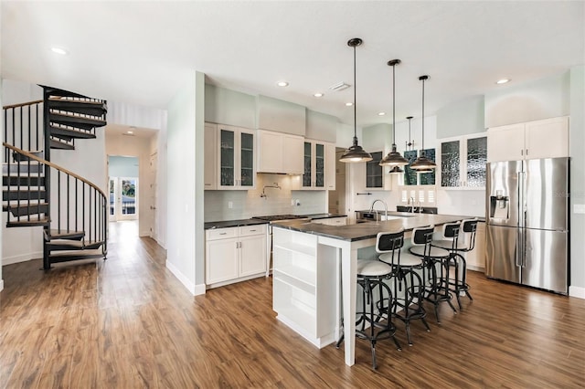 kitchen with stainless steel fridge, dark wood-style flooring, backsplash, dark countertops, and a kitchen island with sink