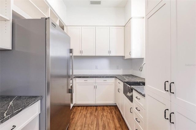 kitchen with freestanding refrigerator, white cabinetry, dark stone countertops, and wood finished floors