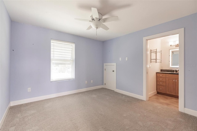 unfurnished bedroom with baseboards, a sink, ceiling fan, light carpet, and ensuite bathroom