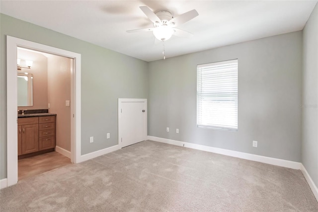 unfurnished bedroom with connected bathroom, baseboards, light colored carpet, and ceiling fan