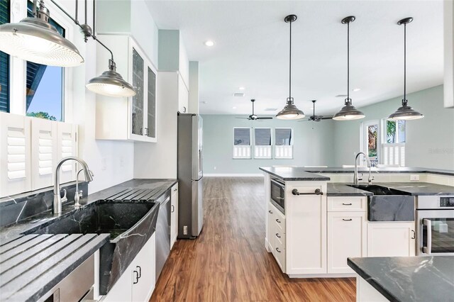kitchen with a sink, pendant lighting, wood finished floors, appliances with stainless steel finishes, and glass insert cabinets