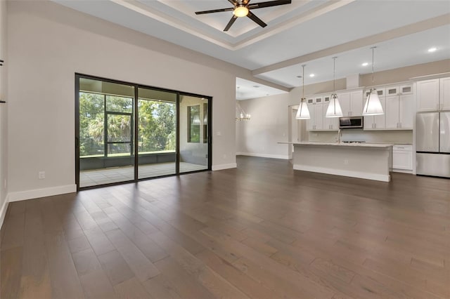 unfurnished living room featuring ceiling fan with notable chandelier and dark hardwood / wood-style flooring