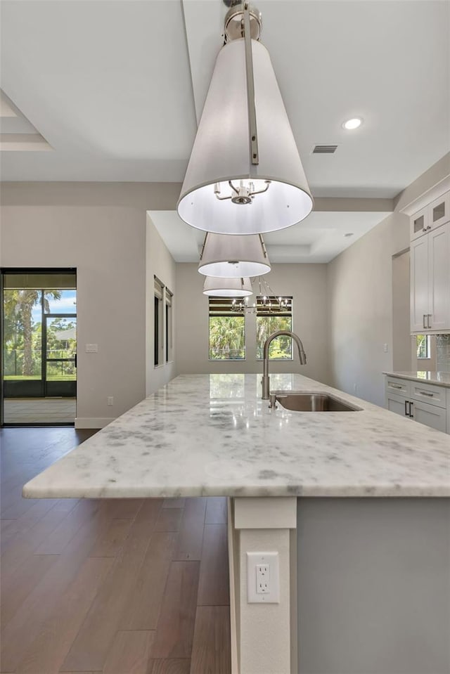 kitchen with a kitchen island with sink, dark hardwood / wood-style flooring, light stone countertops, white cabinets, and sink