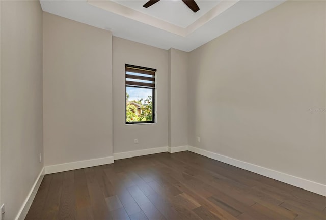 empty room featuring a ceiling fan, dark wood-style flooring, a raised ceiling, and baseboards