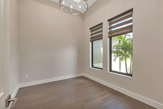 spare room featuring baseboards, dark wood finished floors, and a notable chandelier