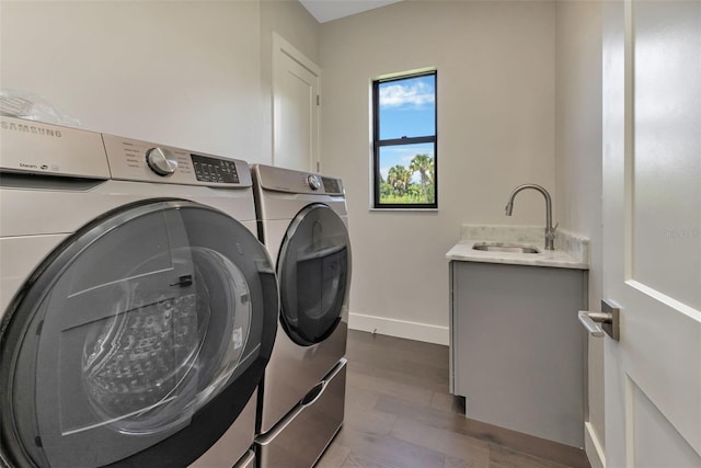 clothes washing area featuring cabinets, washer and clothes dryer, hardwood / wood-style flooring, and sink