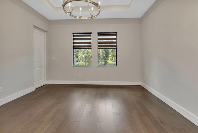 empty room with a chandelier, a tray ceiling, dark wood finished floors, and baseboards