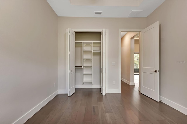 unfurnished bedroom featuring dark wood-style floors, a closet, visible vents, and baseboards