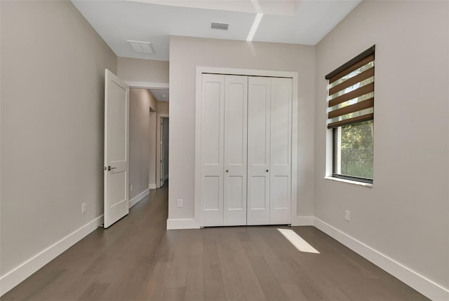 unfurnished bedroom featuring dark wood-style floors, a closet, visible vents, and baseboards