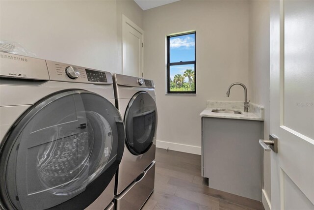 washroom featuring washer and clothes dryer, cabinet space, a sink, wood finished floors, and baseboards