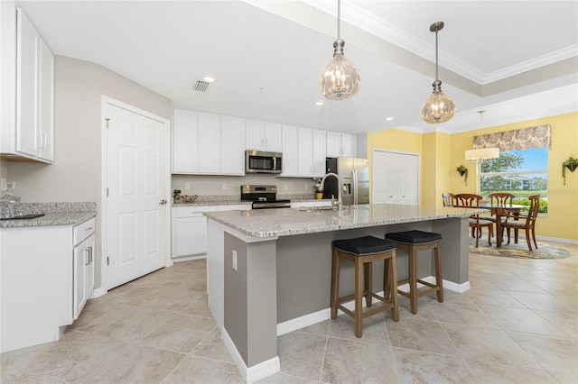 kitchen with appliances with stainless steel finishes, white cabinetry, decorative light fixtures, a center island with sink, and ornamental molding