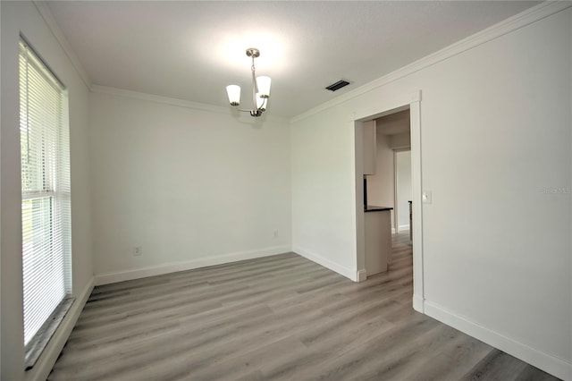 empty room with wood-type flooring, ornamental molding, and a chandelier