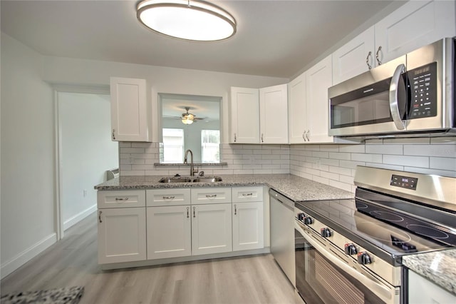 kitchen featuring appliances with stainless steel finishes, decorative backsplash, white cabinetry, light stone countertops, and sink