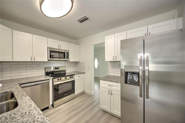 kitchen with white cabinets, appliances with stainless steel finishes, light stone countertops, and light hardwood / wood-style flooring