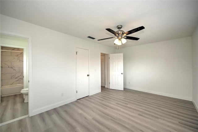 unfurnished bedroom with light wood-type flooring, connected bathroom, ceiling fan, and a textured ceiling