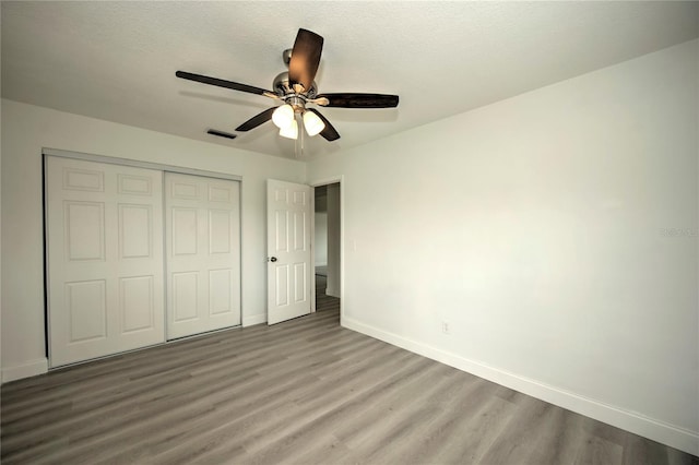 unfurnished bedroom featuring ceiling fan, a textured ceiling, a closet, and wood-type flooring