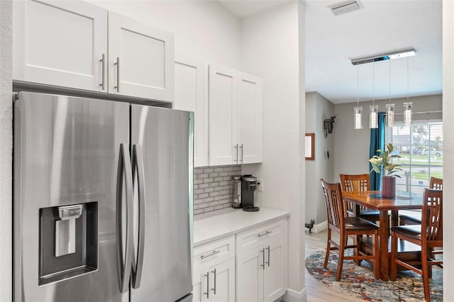 kitchen with hanging light fixtures, stainless steel fridge, backsplash, white cabinetry, and light hardwood / wood-style floors