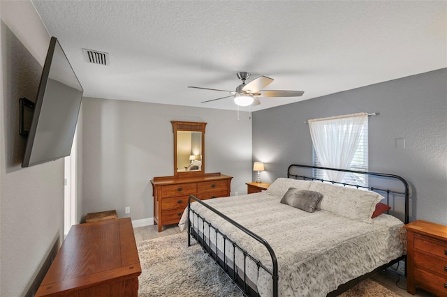 bedroom with ceiling fan, a textured ceiling, and light hardwood / wood-style flooring