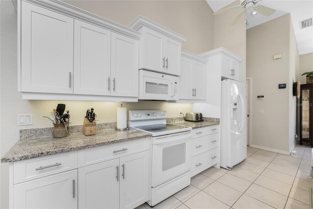 kitchen featuring white appliances, white cabinets, vaulted ceiling, light stone countertops, and light tile patterned floors