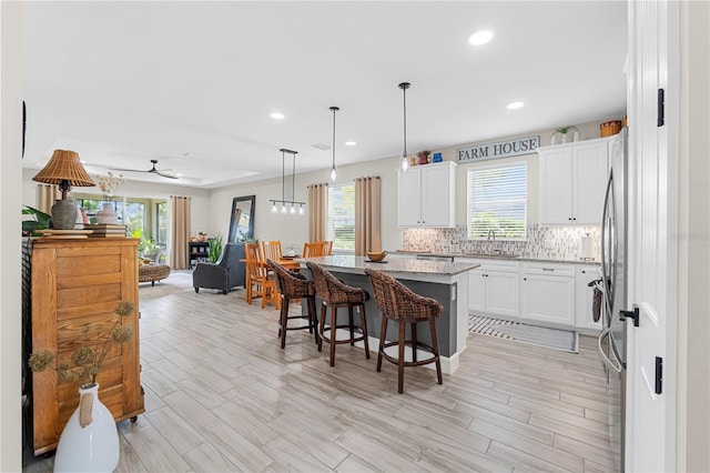 kitchen featuring hanging light fixtures, sink, backsplash, white cabinetry, and a center island