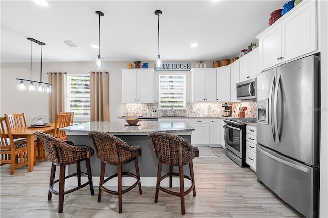 kitchen featuring a center island, white cabinetry, stainless steel appliances, decorative light fixtures, and light stone countertops