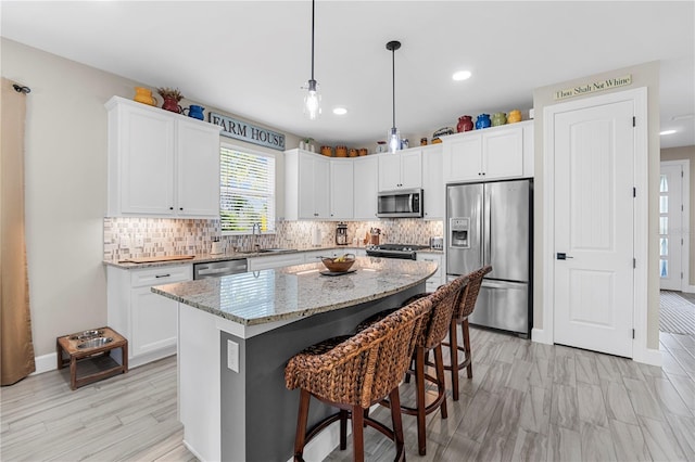 kitchen with light stone counters, white cabinets, sink, a kitchen island, and stainless steel appliances