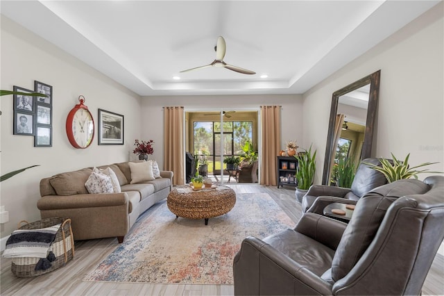 living room featuring light wood-type flooring, a raised ceiling, and ceiling fan