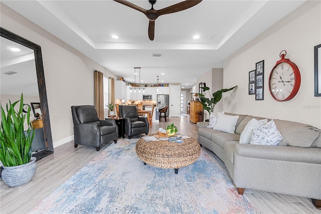 living room with ceiling fan, light wood-type flooring, and a tray ceiling