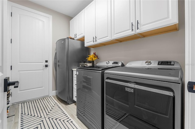 laundry area featuring washing machine and clothes dryer, light hardwood / wood-style flooring, and cabinets