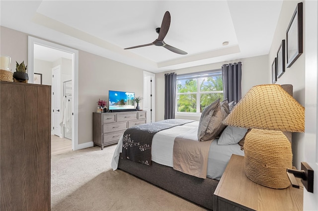 bedroom featuring a tray ceiling, light carpet, ceiling fan, and ensuite bath