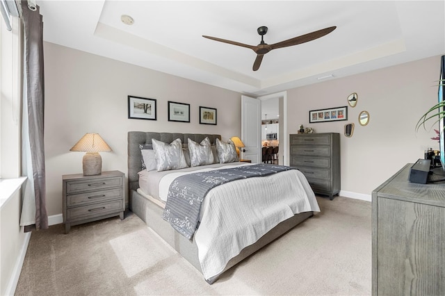 bedroom with light carpet, ceiling fan, and a raised ceiling