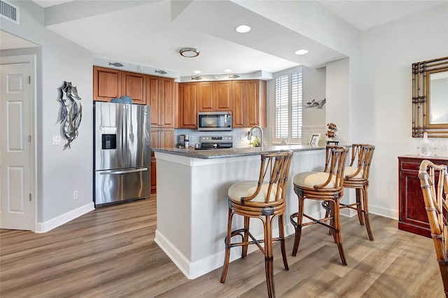 kitchen with kitchen peninsula, backsplash, a kitchen breakfast bar, appliances with stainless steel finishes, and light hardwood / wood-style floors