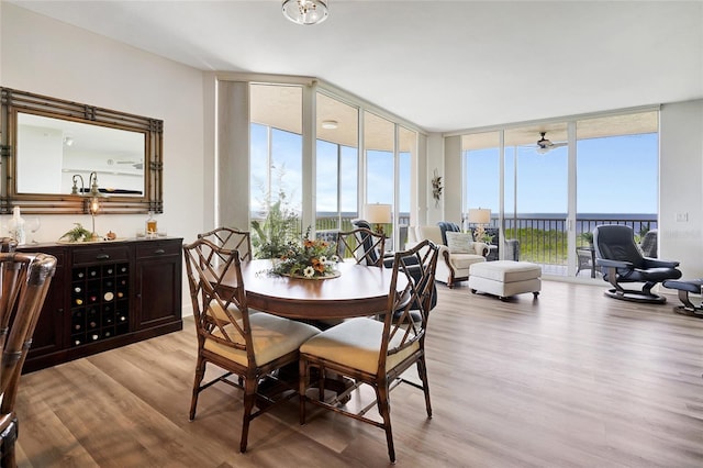 dining room featuring a water view, floor to ceiling windows, light hardwood / wood-style flooring, and ceiling fan